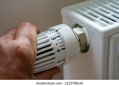 Rising heating costs in the crisis: Man regulates the temperature at home with the heating thermostat to save energy, close up with hand - Shutterstock ID 2153788145
