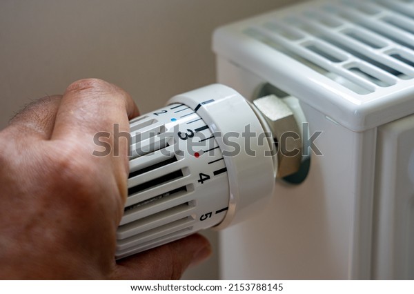 Rising heating costs in the crisis: Man regulates\
the temperature at home with the heating thermostat to save energy,\
close up with hand