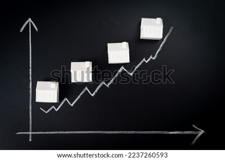 Rising house prices concept metaphor shown from plastic miniature houses and line graph on black board
