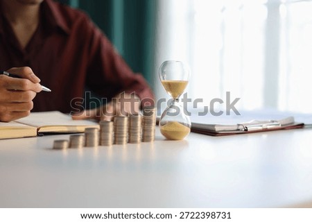 Rising stack of coins and running sand clock on the table. Growing of income, saving or return investment through time. Time and money concept.