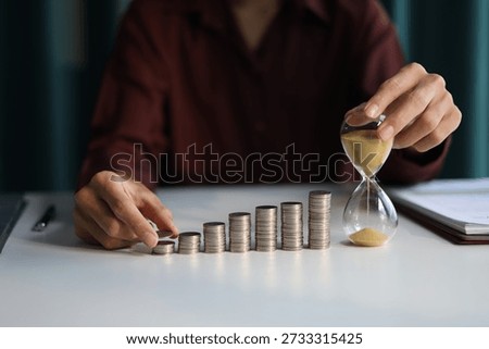 Rising stack of coins and running sand clock on the table. Growing of income, saving or return investment through time. Time and money concept.