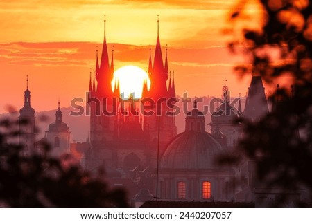 The rising sun in between towers of the Church of Our Lady before Tyn in UNESCO site Prague seen through leaves.