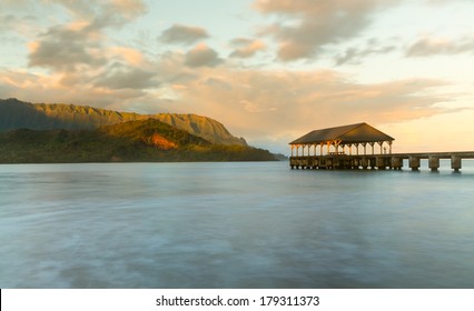 Rising sun illuminates the peaks of Na Pali mountains over the calm bay and Hanalei Pier in long exposure photo - Powered by Shutterstock