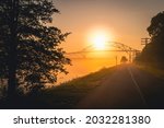 The rising sun over Shining Sun Bikeways along Cape Cod Canal with the view of Bourne Bridge in illuminated soft fog