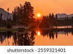 The rising sun shines through wildfire smoke from up North on calm, reflective Sprague Lake in Rocky Mountain National Park, Estes Park, Colorado