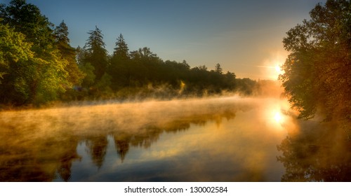 The Rising Sun Shining On A Misty Lake With Forest In Background