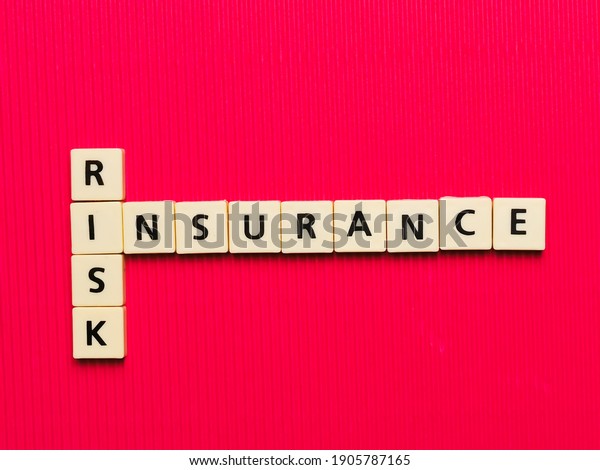 RISK INSURANCE crossword\
made from square letter tiles on red background.Business\
concept.