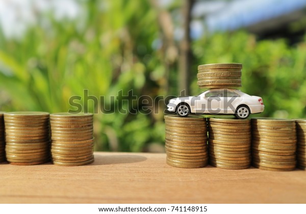 Risk investment concept, miniature white car\
carry coins on rolls of gold money and empty space on wood table in\
blur natural tree and bright\
light