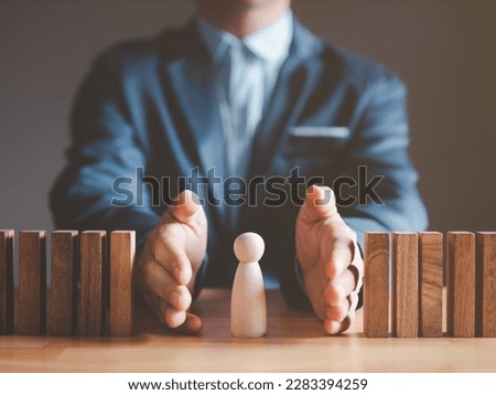 Risk management and assessment concept. Businessman prevent or protect his business and employee from high risk. Wood block represent of risk attack to business, two hands block and protect the domino