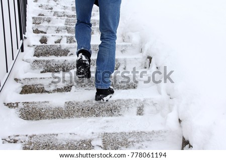 Risk of slipping when climbing stairs in winter. A man goes up a snow-covered staircase