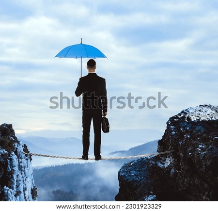 Risks and challenges of entrepreneurship. Businessman with portfolio and umbrella standing on rope over abyss in mountains, back view