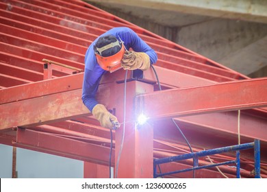 Risky welder while climbing and welding on top of the steel roof structure work at the building construction site. Skilled worker is welding on the high steel structure at the construction project.
