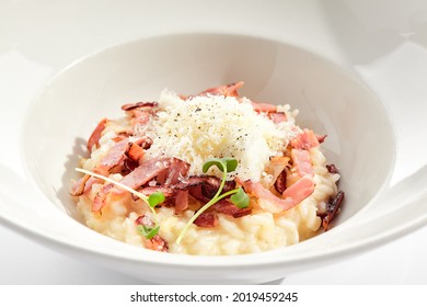 Risotto alla carbonara on white restaurant plate. Risotto with bacon and egg, garnished with micro greens. Risotto topped with parmesan cheese