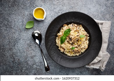 Risotto with mushrooms in a black plate over gray background, top view