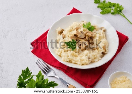 Risotto with mushrooms garnished with parsley in a light plate on a white concrete background. Risotto recipes. Italian Cuisine