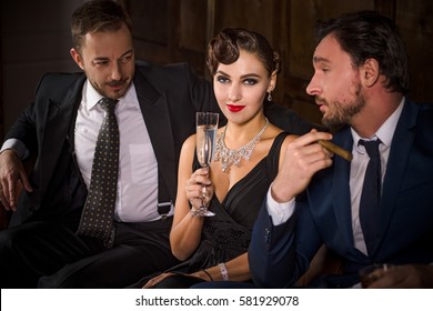 Rivalry or competition between two handsome rich executive men for elegant lady with red lips. Pretty lady sitting with glass of champagne. Richness, wealth, luxury concepts.