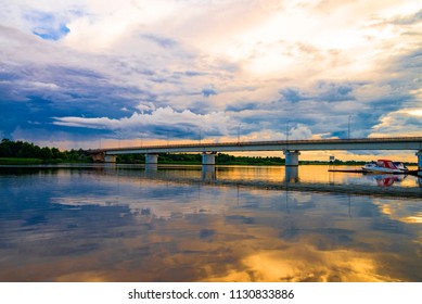 river and bridge on sunset background. Bright orange and yellow sky illuminates a bridge crossing the still river.
