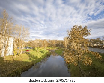 River with a bridge over it and trees in the background. The sky is cloudy and the sun is shining through the clouds