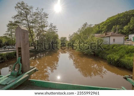 A river with chocolate-colored water with the sun reflecting in it in a foggy sky. Spring 