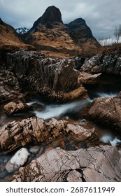 The River Coe flows through Glen Coe with The Three Sisters mountains in early spring, Scotland
