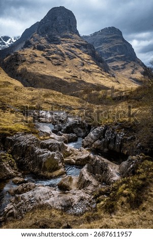 The River Coe flows through Glen Coe with The Three Sisters mountains in early spring, Scotland