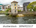 River Corrib with flowing water and the Galway Fishing Watchtower Museum with buildings in the background, Waterways of Galway,, cloudy day in Galway city, Connacht province, Ireland