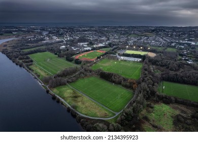 River Corrib Flows Into Galway City, Aerial View. Sport Ground With Tall Goal Posts For Irish National Sport On The Right. Training Field For Hurling, Rugby, Camogie, Gaelic Football. Dusk Time.