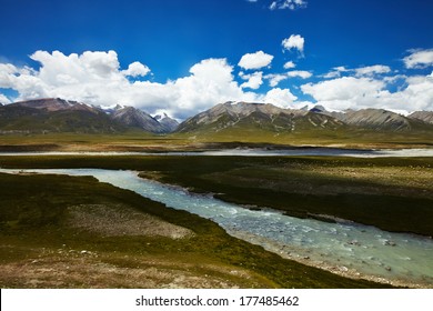 A river cross a plains in Tibetan Plateau, with mountain landscape and cloudy sky