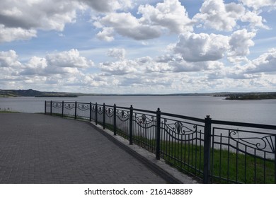 River Embankment. Metal Fencing. Blue Sky With White Clouds.