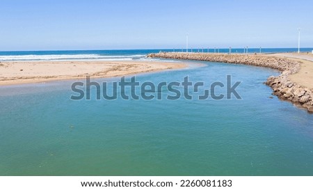 River estuary mouth water flowing out into blue ocean sea  along beach coastline on a summer day.