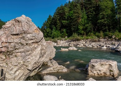 River Gail flowing through the Schuett in the natural park Dobratsch in Villach, Carinthia, Austria. Gailtaler and Villacher Alps. Riverbank is full of massive rocks. Swimming in crystal clear water