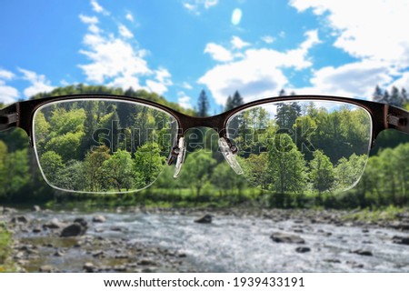 River and green forest landscape focused in women's glasses frame. View through eyeglasses. Better vision concept. Colorful view of sunset landscape in glasses. 