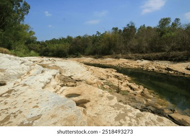 A river landscape surrounded by limestone rocks, tall green trees with a bright blue sky in the background. - Powered by Shutterstock