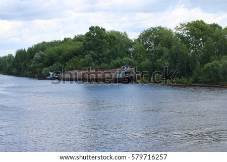 River with lonely rusty cargo ship dire straits among bushes and trees on summer day
