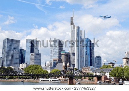 River - Main with european city skyline. Airliner is flying, Jet plane in high flight. Skyscraper buildings in Germany on blue sky background. Business and Financial Center Frankfurt Main. Travel 
