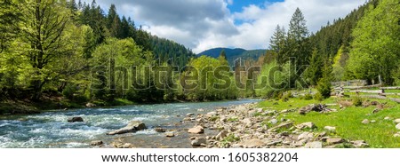 river in mountains. wonderful springtime scenery of carpathian countryside. blue green water among forest and rocky shore. wooden fence on the river bank. sunny day with clouds on the sky