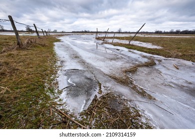 River Partially Frozen In Winter, Sunset, Road Flooded With Water And Frozen