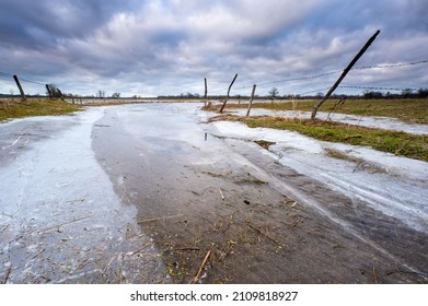 River Partially Frozen In Winter, Sunset, Road Flooded With Water And Frozen