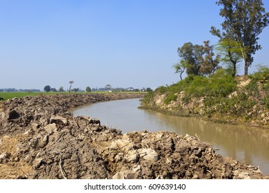 A River In Punjab India With Piled Up Earth And Trees Under A Blue Sky