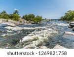 River rapids in eastern Canada featuring running clear water, pink limestone, green forest on a sunny day