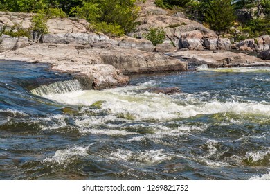 River rapids in eastern Canada featuring running clear water, pink limestone, green forest on a sunny day