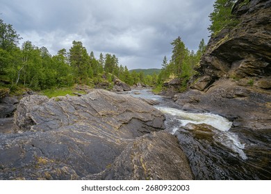 River with rapids flowing between large rocks and forest in Norwegian wilderness under cloudy weather