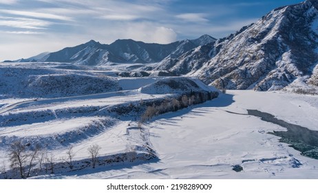 A River In A Snowy Valley. The Central Part Of The Riverbed Is Not Frozen. Steam Rises Above The Water. A Picturesque Mountain Range Against The Blue Sky. Altai. Katun