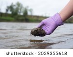 River soil composition concept. Woman a scientist takes a sludge sample from a river close up.
