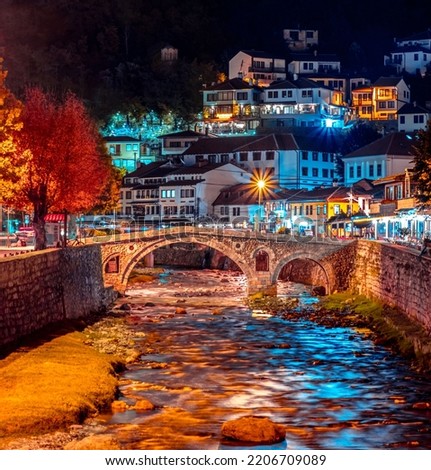 A river with a stone bridge in downtown Prizren with buildings and trees at night, Pristina Kosovo