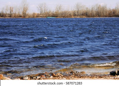 River Stones In Forest River Landscape. Water Surface With Ripples And Sunrays Reflection. Summer River Shore Landscape