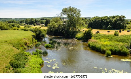 The River Stour runs through fields of pasture and hay bales in the agricultural landscape of Dorset's Blackmore Vale, with Shillingstone Station and the wooded hills of the Dorset Downs behind. - Shutterstock ID 1617708571