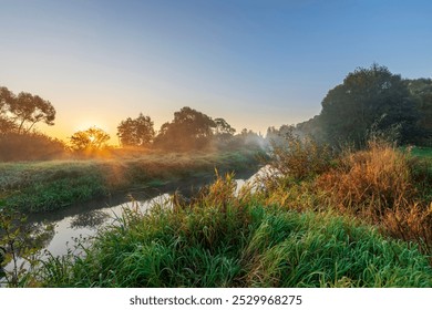 A river with a sun setting in the background. The sky is blue and the sun is orange