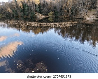 river surface reflections and ripples creating mirrorlike texture, gentle trail of waves, overhanging autumn