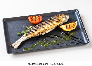 River trout grilled with tomato and lemon on a rectangular plate. Decorated with marjoram and sous